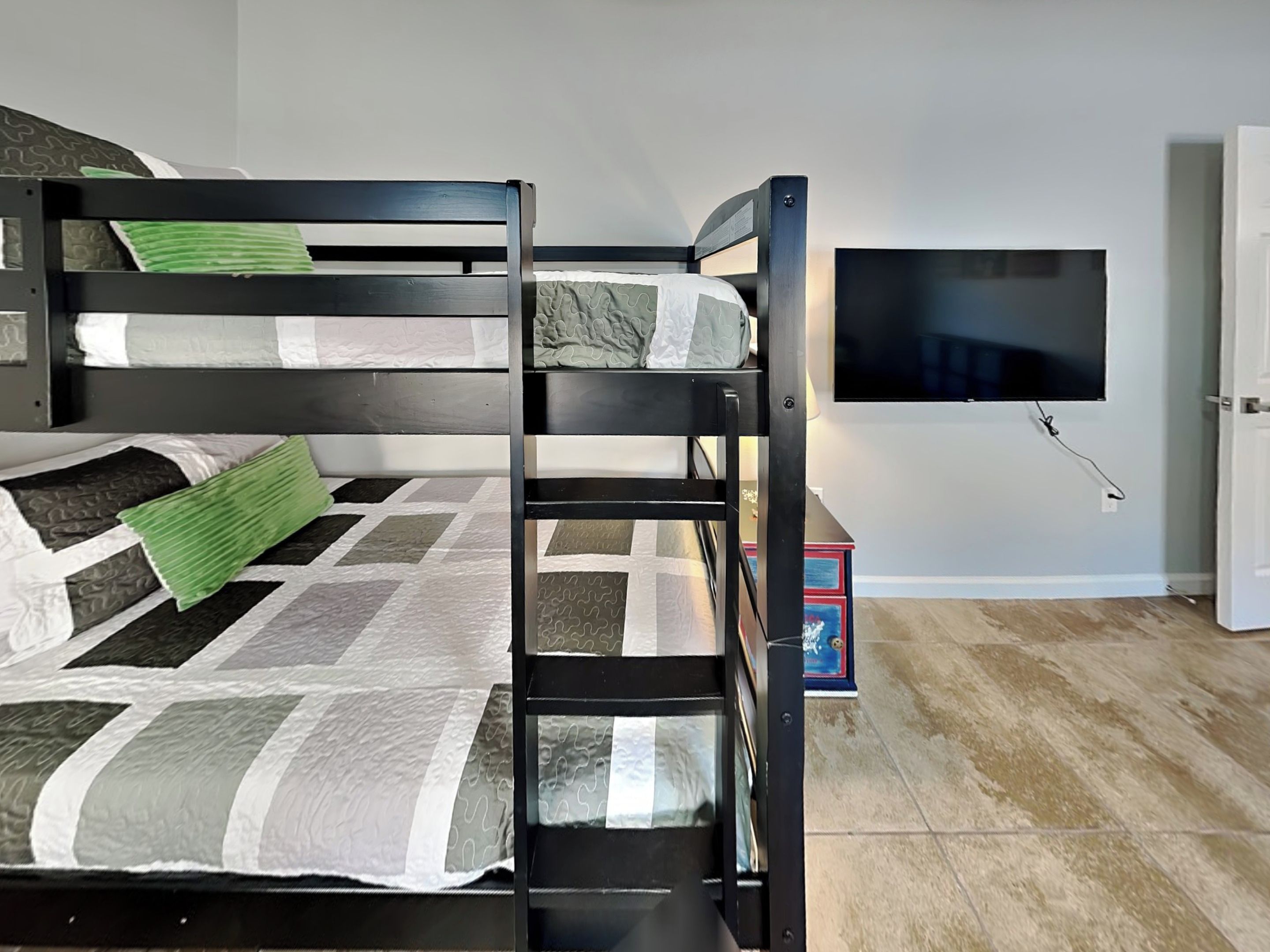 A bunk bed with a television mounted on the wall, a door, and a small table with a box.