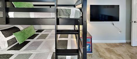 A bunk bed with a television mounted on the wall, a door, and a small table with a box.