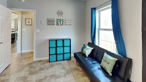 A modern living room with a black leather sofa, teal storage units, and a large window with blue curtains. - Bayside Abode by Miss Kitty’s (Rockport)