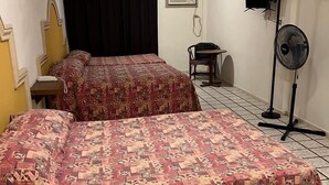 Habitación de hotel con dos camas, un escritorio, una silla, un ventilador y un televisor en la pared.