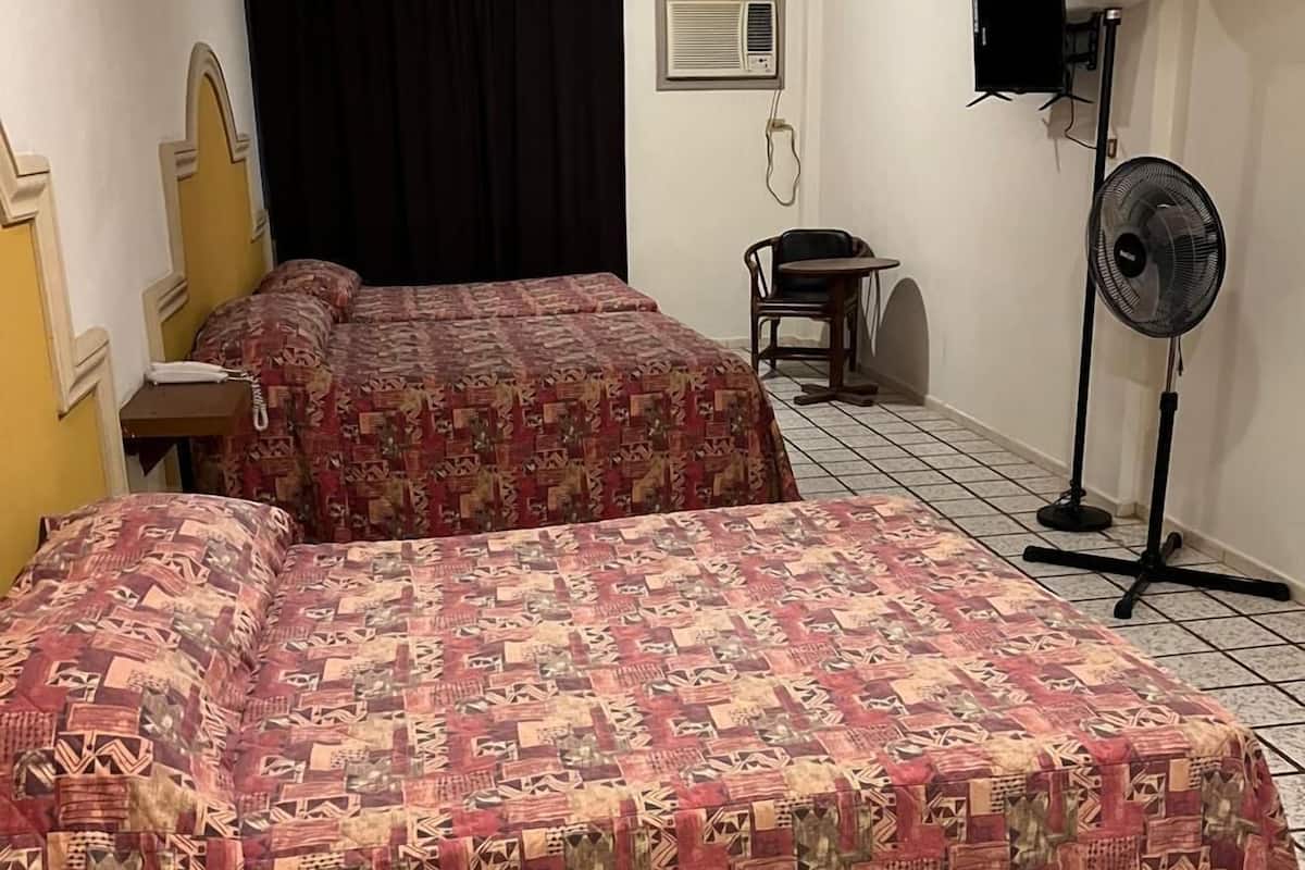 Ein Hotelzimmer mit zwei Betten, einem Schreibtisch, einem Stuhl, einem Standventilator und einem Fernseher an der Wand.