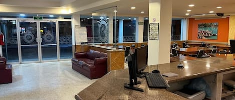 Un vestíbulo de hotel con mostrador de recepción, zona de estar y puerta de vidrio de acceso.