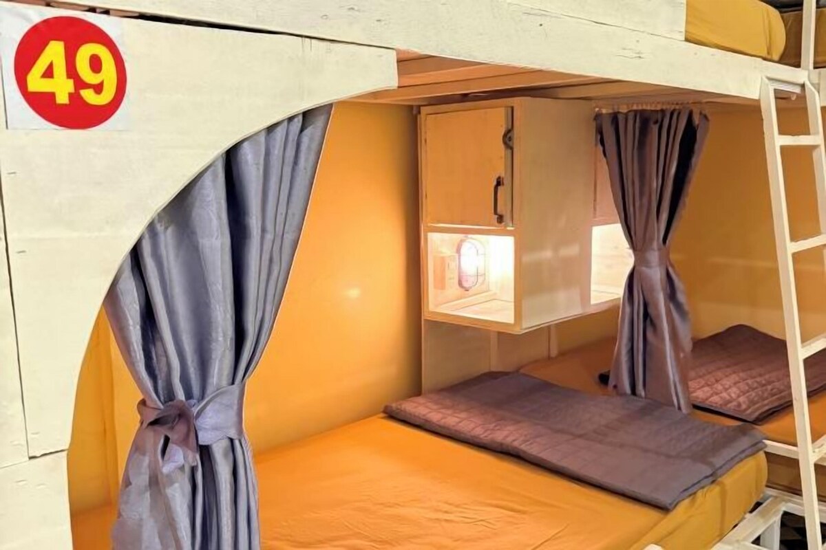 A bunk bed room with curtains, a ladder, and a window with a light fixture.