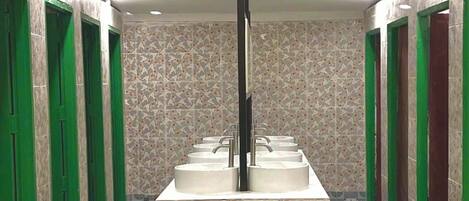 A public restroom with multiple sinks, green doors, patterned floor tiles, and ceiling-mounted lights.