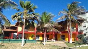 Un bâtiment à la façade rouge et jaune, entouré de palmiers et d’une pelouse bien entretenue.