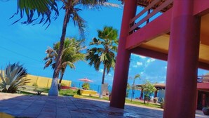 A covered outdoor area with palm trees, a yellow wall, and a clear blue sky. - Beachfront Mansion in Japan, Ceará – A Hidden Treasure 💎" (Japao Aquiraz)