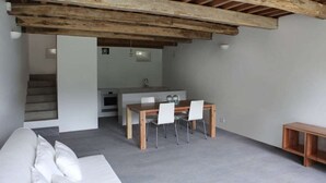 A modern living space with a wooden ceiling, a dining area with a table and chairs, a kitchen area with a sink, and a staircase leading to another level.