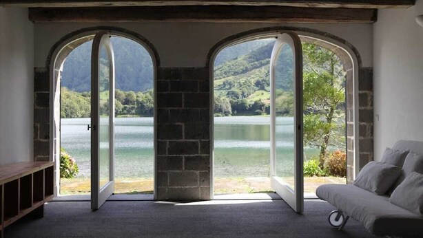 A room with a view of a lake and hills, featuring a sofa and a bench.