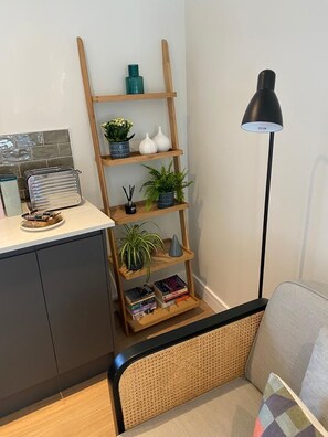 Eine moderne Küche mit einer Holzwandregal, auf der Pflanzen und Bücher stehen, einem Toaster und einer schwarzen Stehlampe.
