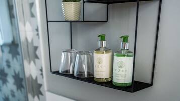 A bathroom shelf with two bottles of Eden hand wash and shampoo, a glass, and a potted plant.