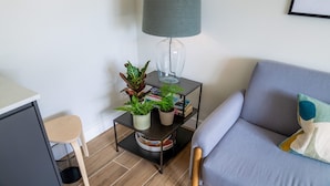 A modern living room with a grey sofa, a small side table with a lamp, and a potted plant.