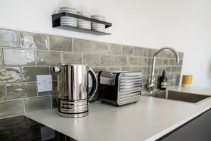 A kitchen with a coffee maker, toaster, and a shelf with containers. - The Den - Small but cosy apartment in the Dales. (Leyburn)
