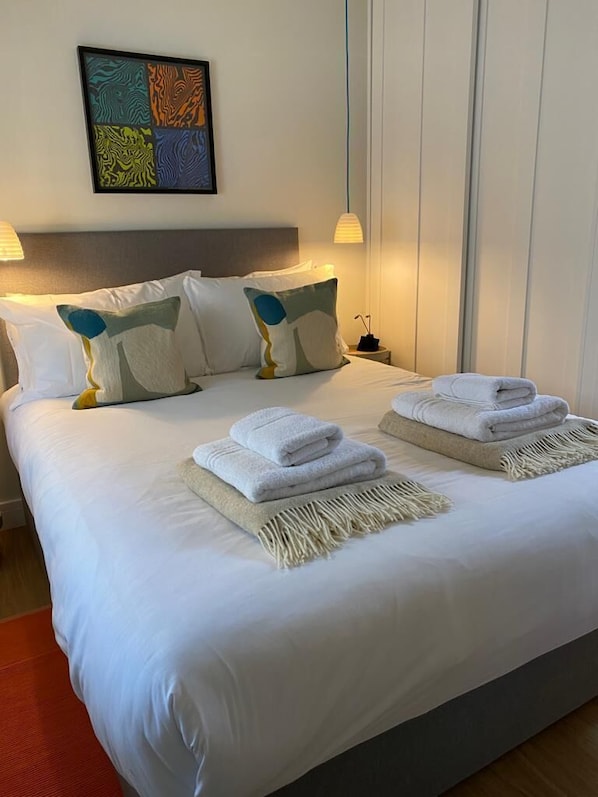 A neatly made bed with white linens, two folded towels, and a decorative pillow. - The Den - Small but cosy apartment in the Dales. (Leyburn)