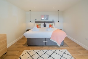 A modern bedroom with a large bed, two bedside tables, a headboard, and a small bedside table with a lamp. - The Den - Small but cosy apartment in the Dales. (Leyburn)