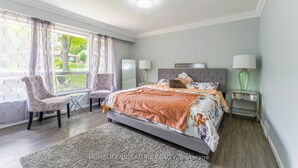 A bedroom with a bed, two chairs, a nightstand, and a window with curtains. - home away home  (Toronto)