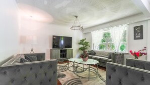 A modern living room with a sofa, armchairs, a glass coffee table, a TV, and a large window with curtains. - home away home  (Toronto)