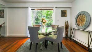 A dining area with a glass table, two upholstered chairs, a vase with flowers, and a clock on the wall. - home away home  (Toronto)