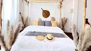 Een bed met hemelbed, decoratieve kussens en een geweven vaas op het nachtkastje.