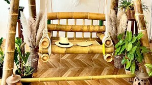 Een schommel van bamboe met een geweven dromenvanger, omringd door potplanten en rustieke decoratie.