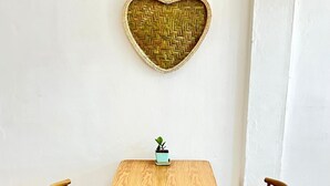 Een houten tafel met twee stoelen, een kleine plant in pot en een geweven hartdecoratie aan de muur.