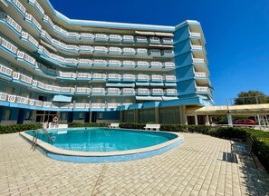 A multi-story hotel with a swimming pool and outdoor seating. - Modern Studio With Shared Pool (Caorle)