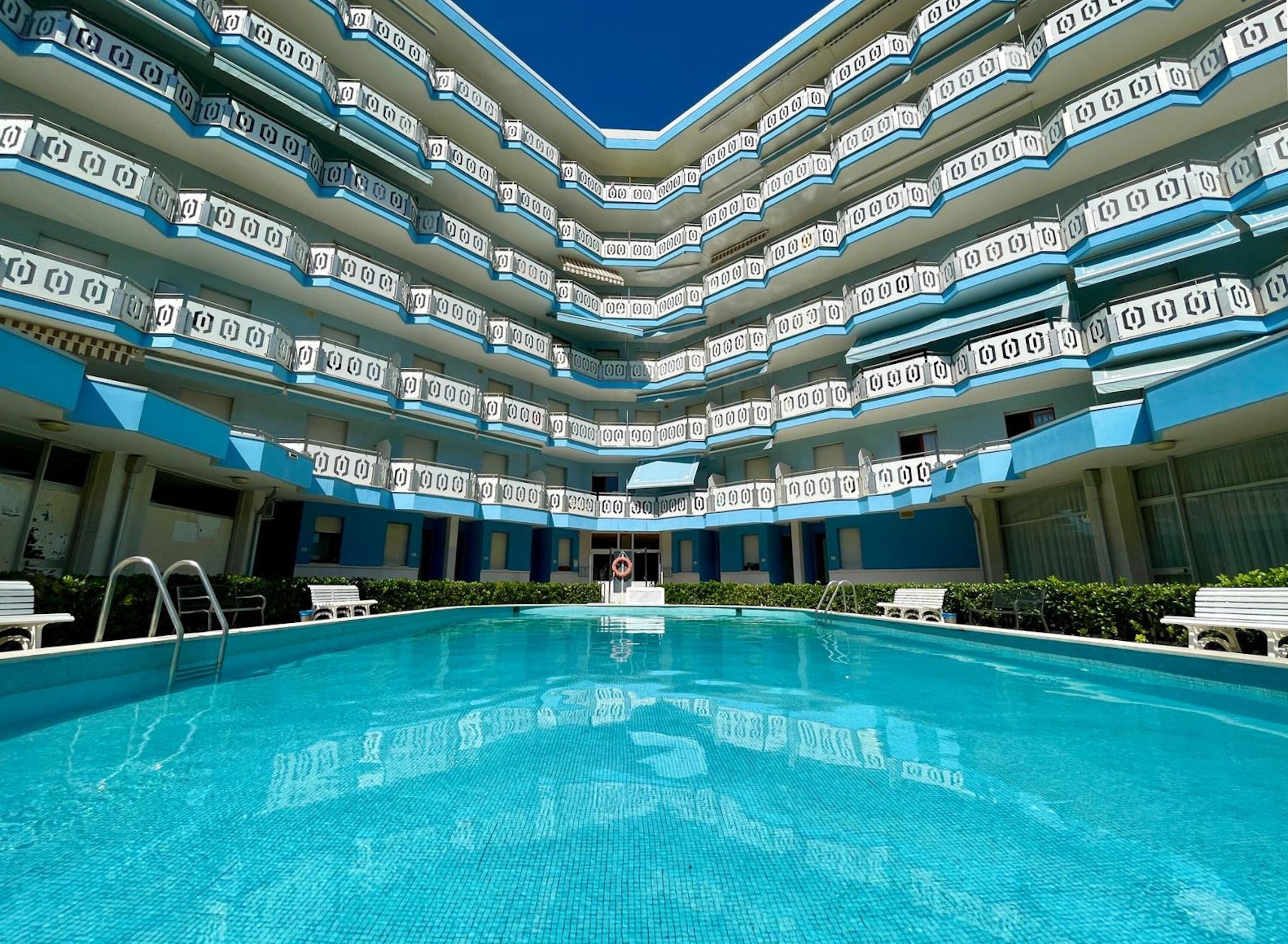 Un hotel con una amplia piscina central, varios balcones y un diseño arquitectónico moderno.
