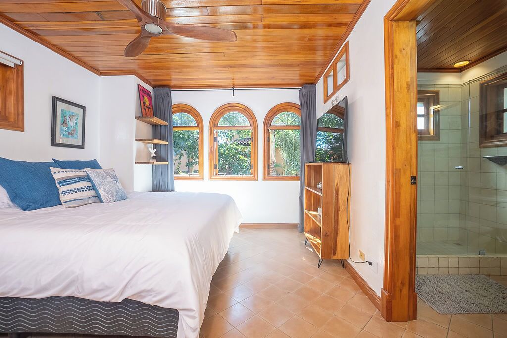A bedroom with a bed, a ceiling fan, a wooden wardrobe, and a shower area.
