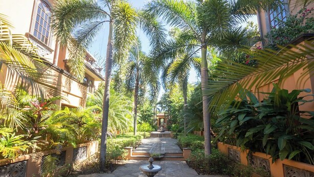 Ein Gartenweg mit einer Fontäne, umgeben von Palmen und üppigem Grün.