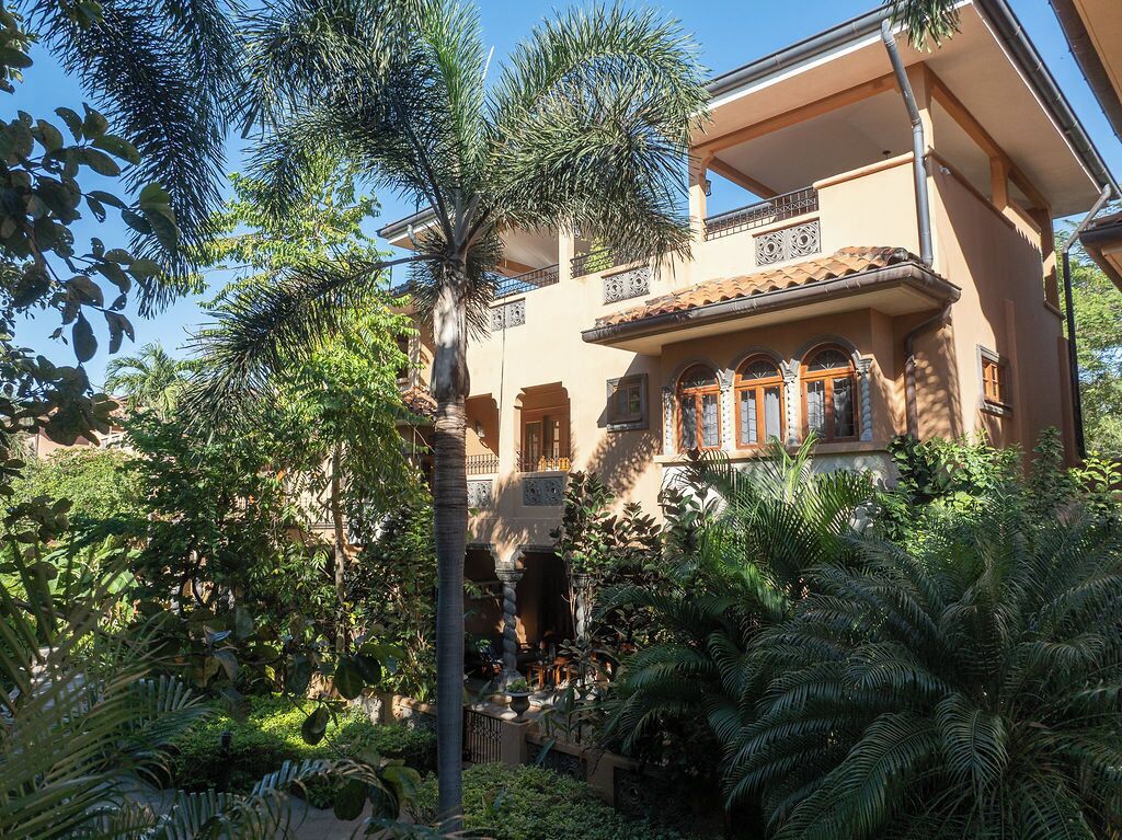 A multi-story building with balconies, surrounded by lush greenery and palm trees.