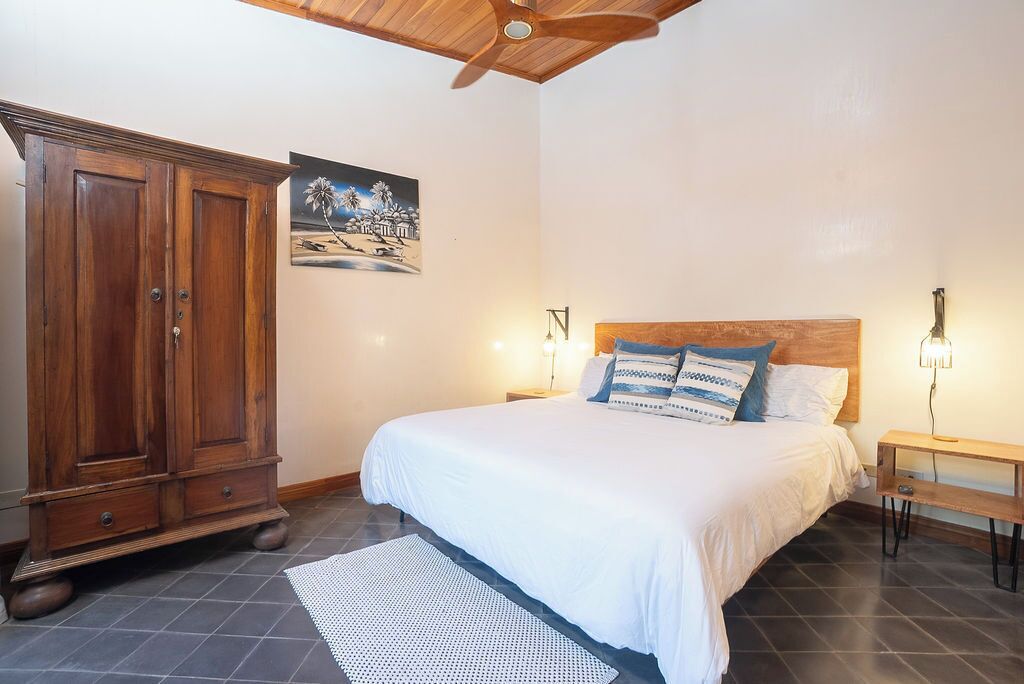 Un dormitorio con un armario de madera, una cama con ropa de cama blanca y un cuadro en la pared.