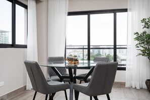 A modern dining area with a glass table and four grey chairs, a decorative globe, and a view of a cityscape through large windows.