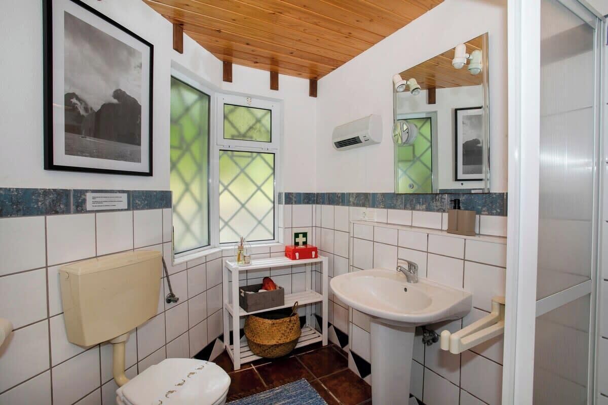 Baño pequeño con inodoro, lavamanos y ventana con vistas a montañas.