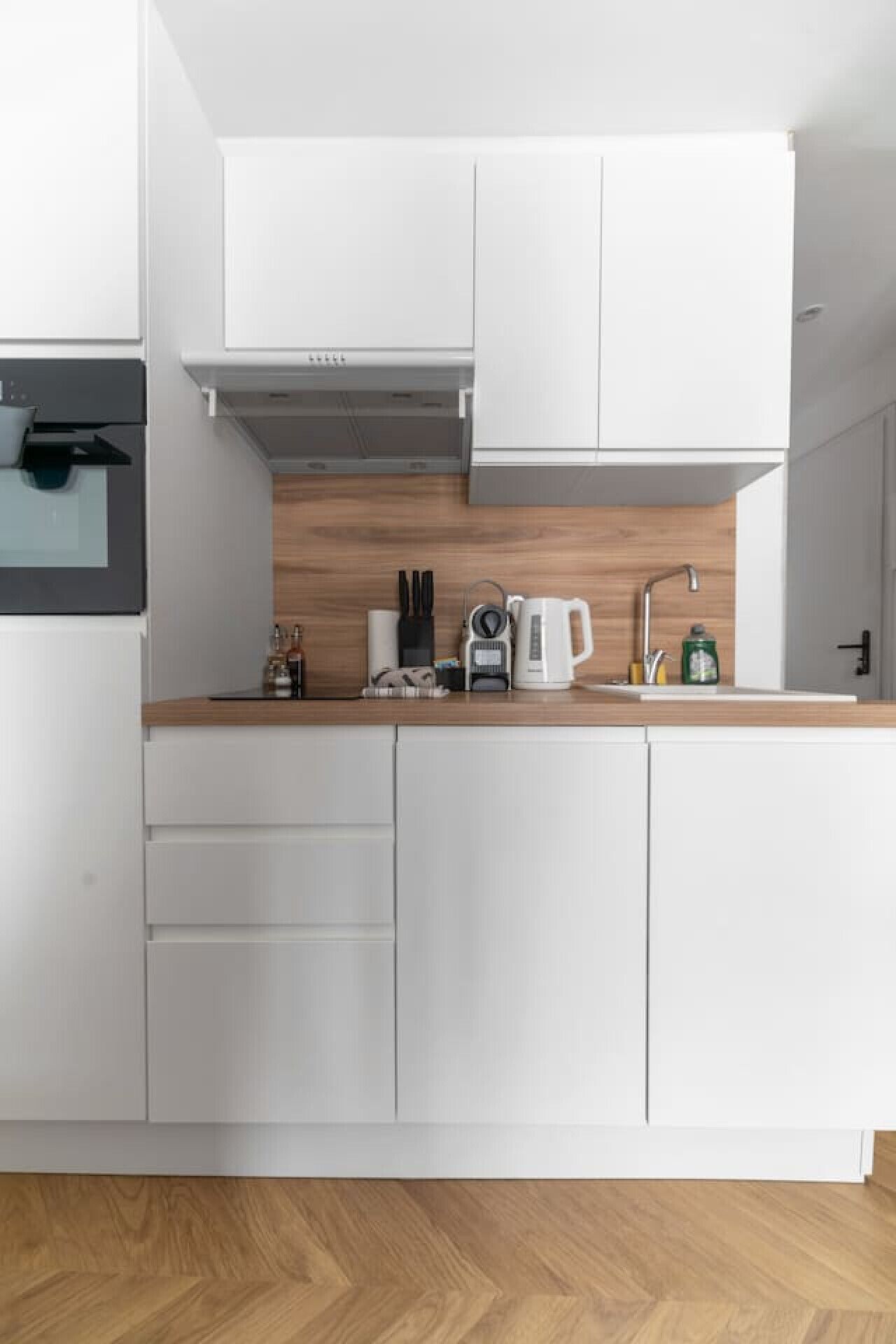 A modern kitchen with white cabinets, a wooden countertop, and a built-in range hood.
