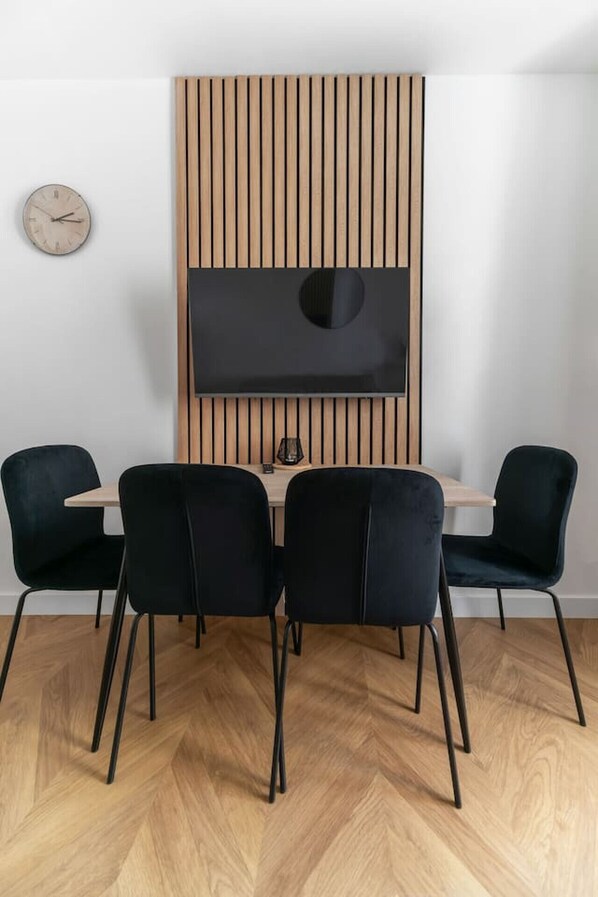 A modern dining area with a wooden slat wall, a flat-screen TV, and black upholstered chairs.
