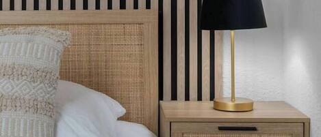 A neatly made bed with a patterned pillow, a bedside lamp, and a wooden nightstand with a woven basket drawer.