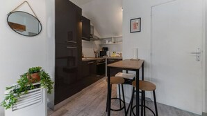 Eine kleine Küche mit dunklen Schränken, einem Essbereich mit Sitzhocker und einem Blumentopf.