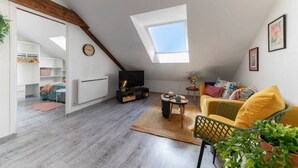 Ein Schlafzimmer im Loft-Stil mit Dachfenster, einem Bett mit floraler Bettwäsche, einem Fernseher und einem gelben Sofa.