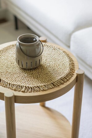 A round wooden table with a woven placemat and a ceramic mug on it.