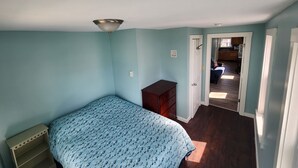 A bedroom with a bed, dresser, and a door leading to a hallway. - G St Inn Unit 5 Lovely 1-bedroom apartment in Hampton with AC, WiFi (Hampton)