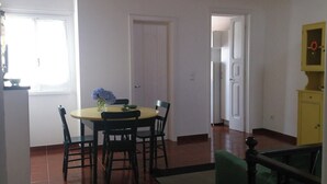 A dining area with a round table, four chairs, a vase with flowers, and a window with curtains.
