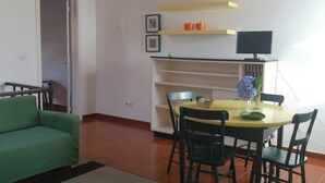 A dining area with a round table, four chairs, a green sofa, and a TV on a shelf.