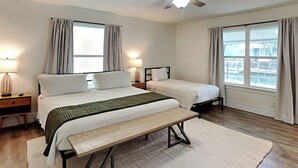 Ein Schlafzimmer mit zwei Betten, einer Bank und Blick auf die Stadt durch große Fenster.