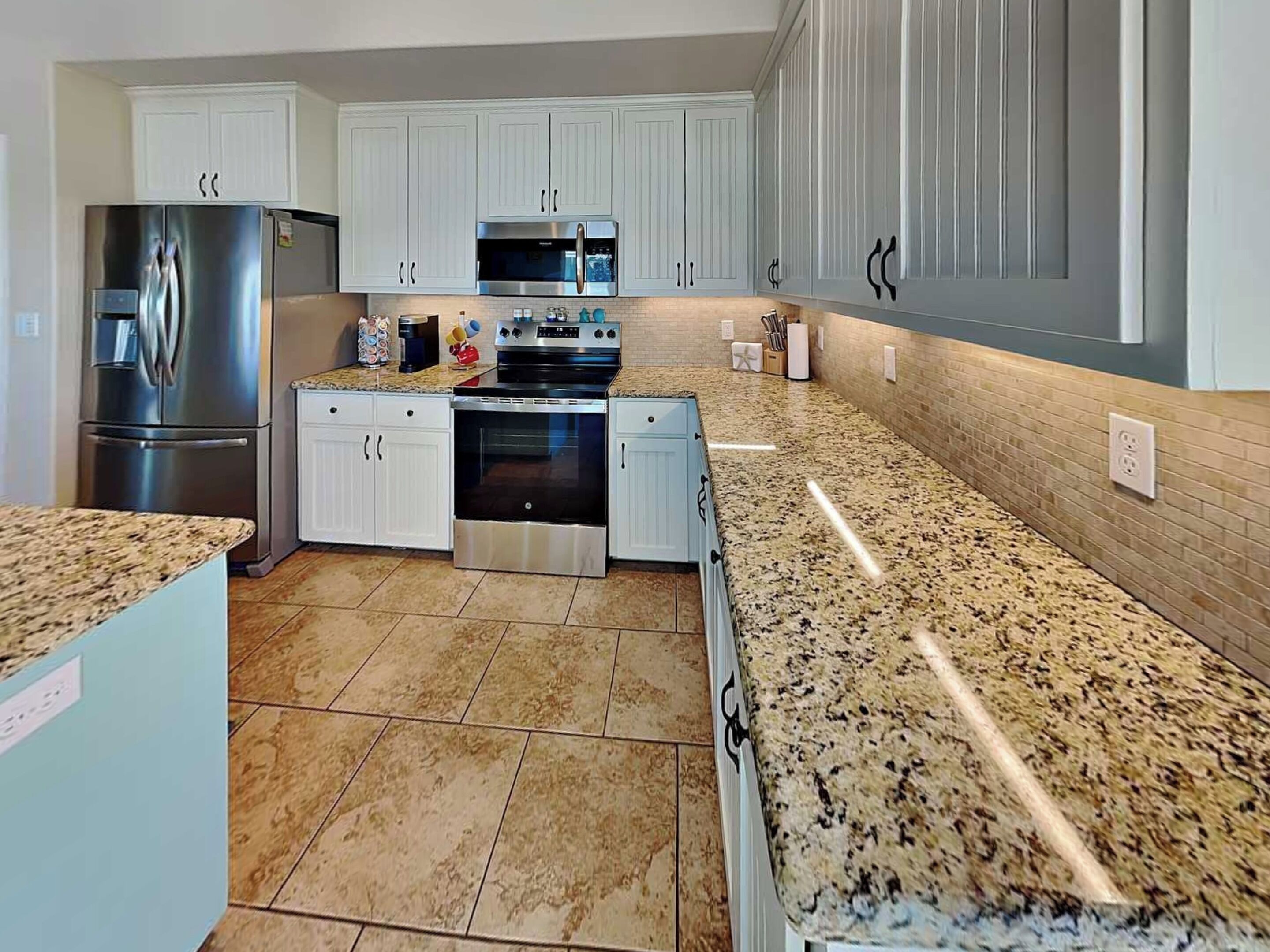 Cozinha moderna com armários brancos, eletrodomésticos de aço inoxidável, bancadas de granito e piso ladrilhado.