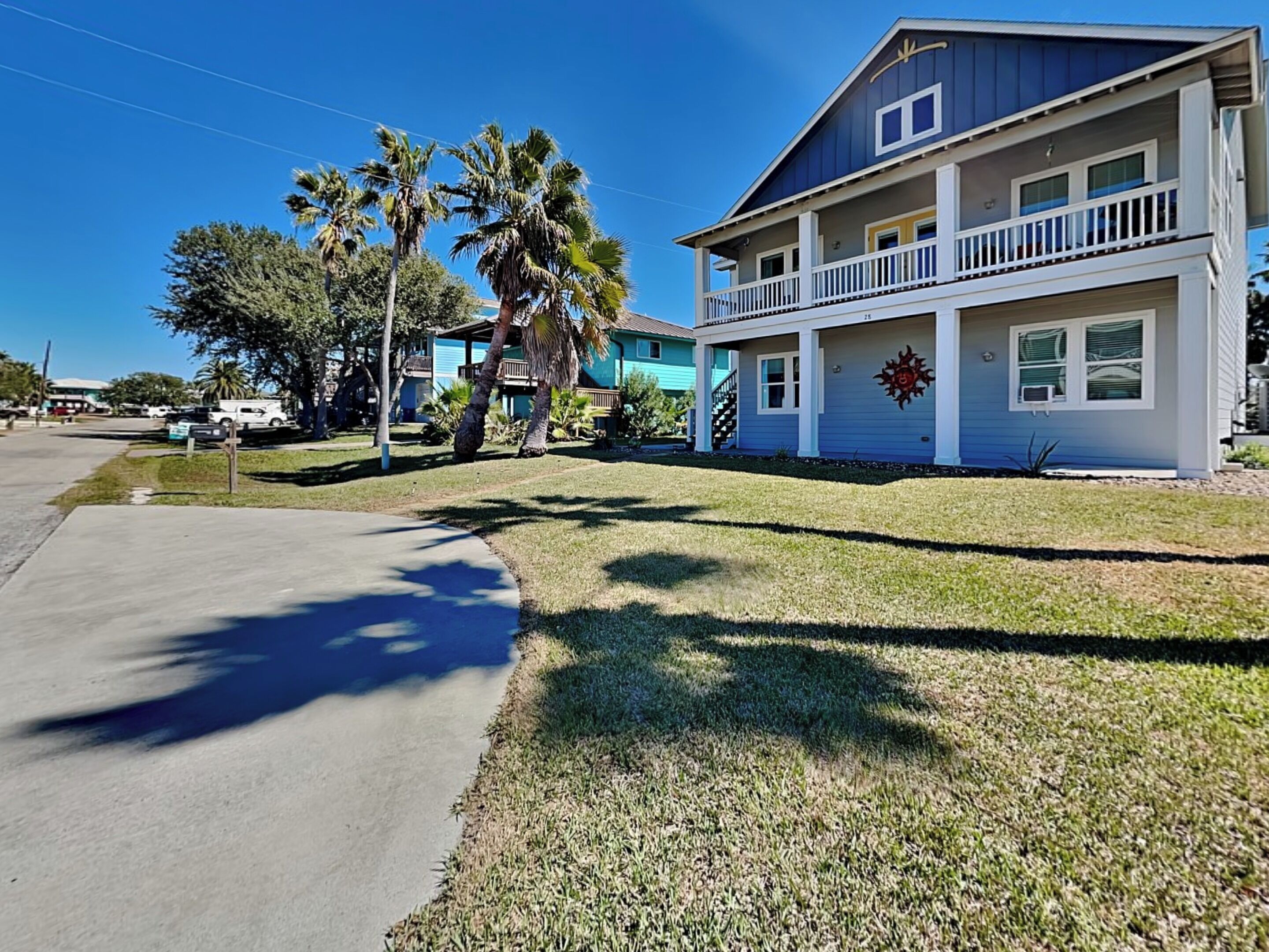 A two-story house with a balcony, surrounded by palm trees and a well-maintained lawn.