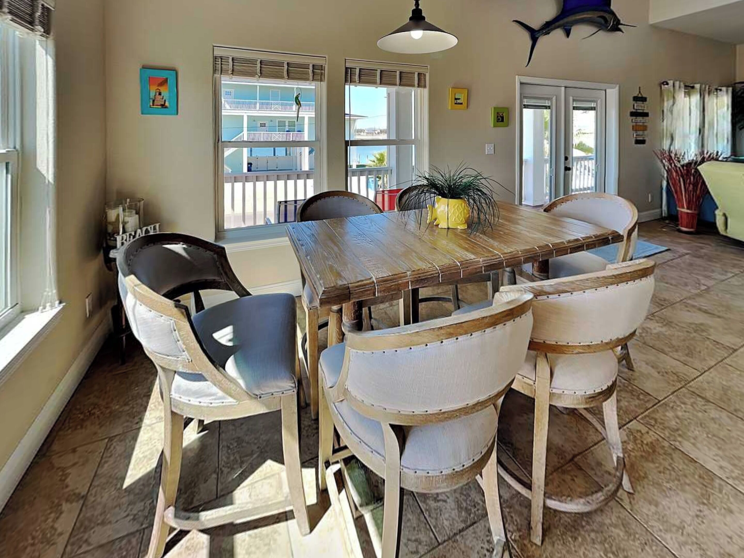 A dining area with a wooden table and four chairs, a hanging light fixture, and a view of a balcony with a railing.