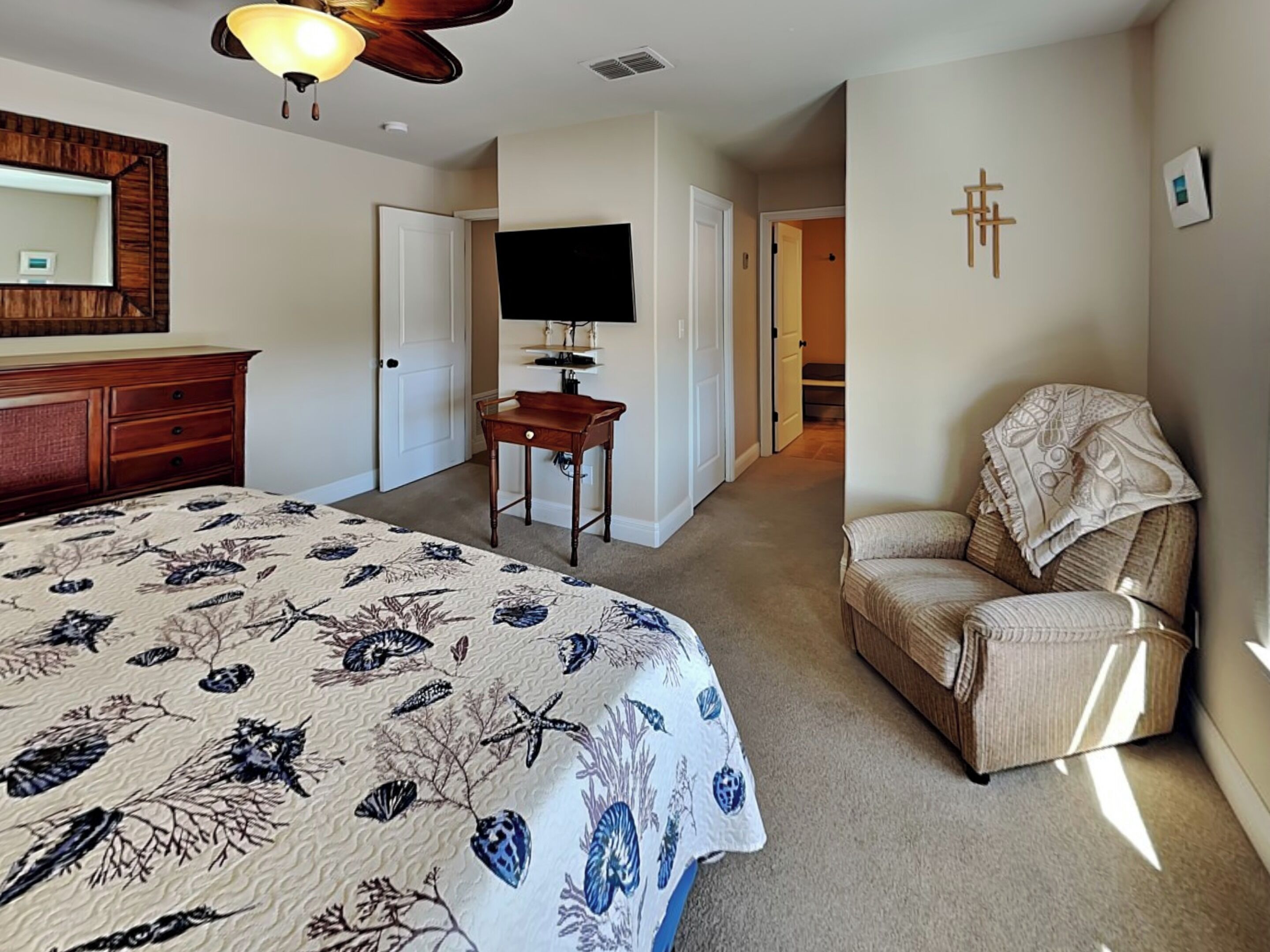 A bedroom with a bed, a desk, a chair, a television, and a door leading to another room.