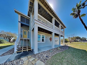 A two-story house with a balcony, a front porch, and a stone pathway leading to the entrance. - Island Charm by Miss Kitty’s (Rockport)