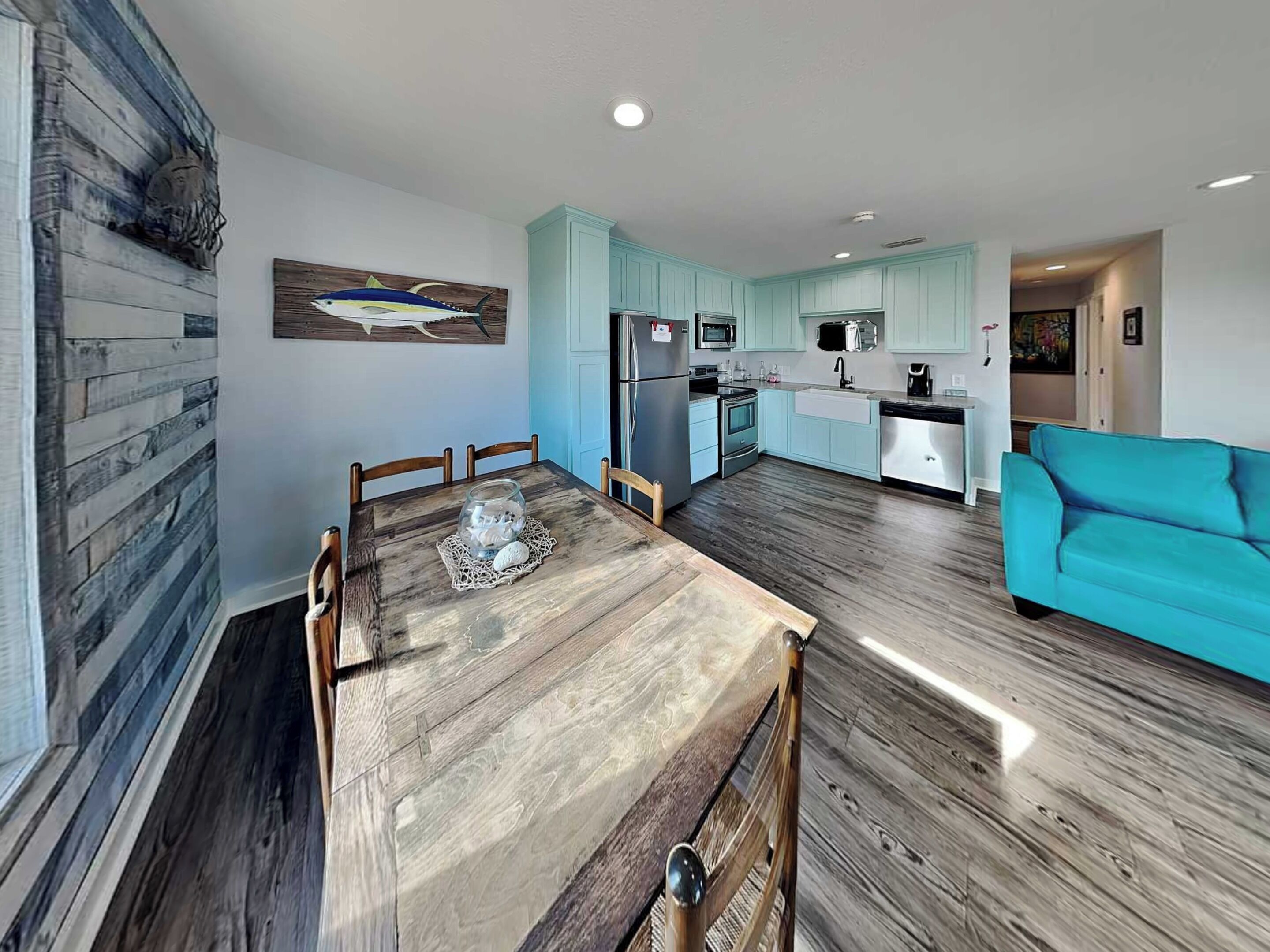 A modern kitchen with light blue cabinets, a dining table with chairs, and a teal sofa in a spacious living area.