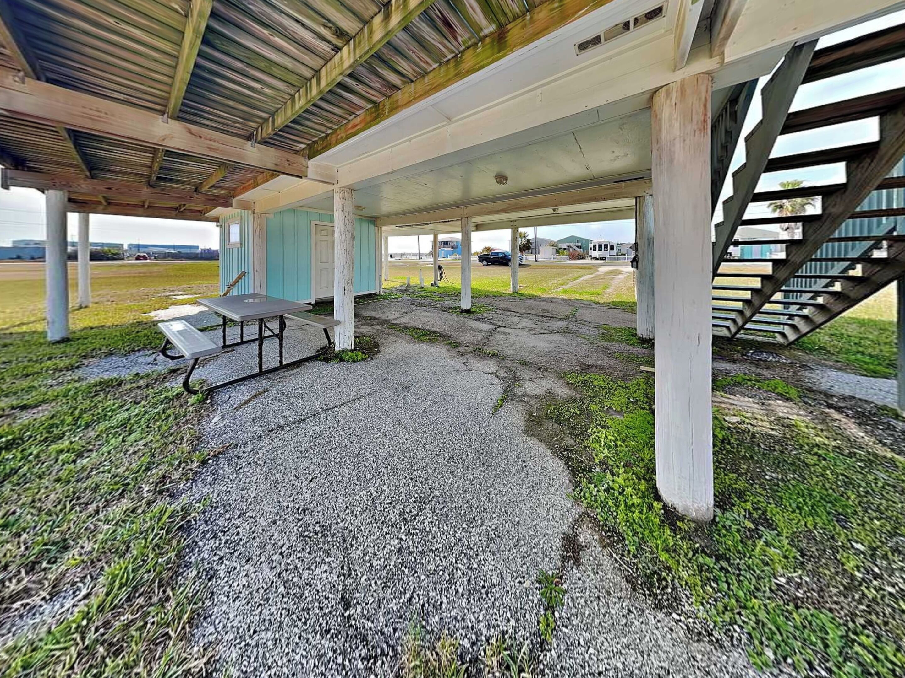 Un espace ext érieur abrité, doté d’une table de pique-nique, d’un sol en béton et d’un escalier menant à un niveau supérieur.