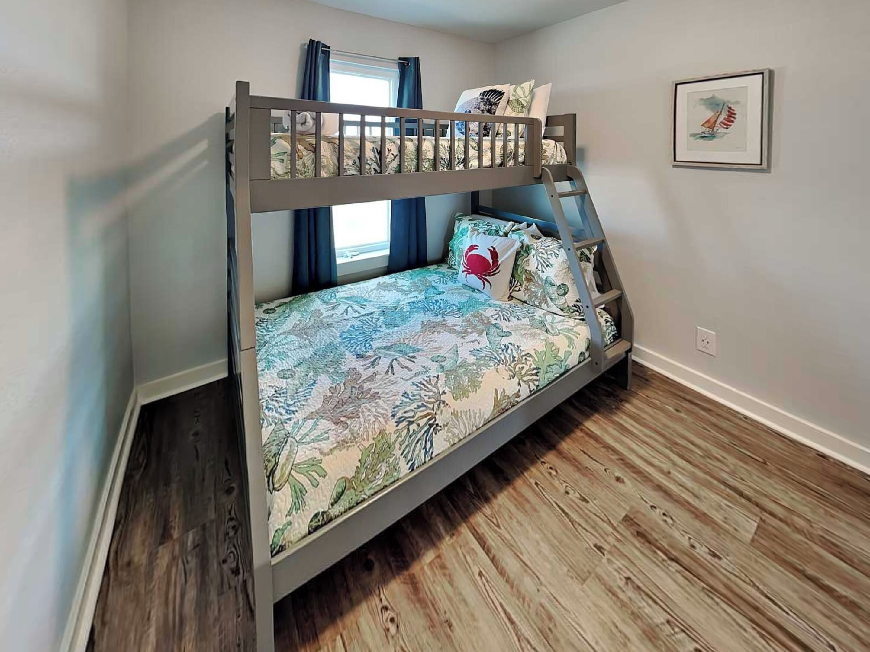 A bunk bed with a floral bedspread, a single pillow with a crab design, and a framed picture on the wall.